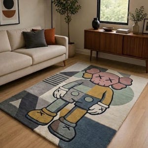 May include: A rectangular rug with a cartoon character design in grey, blue, yellow, and pink. The rug is placed on a wooden floor in a living room, with a sofa and artwork in the background. The rug's design is modern and geometric.