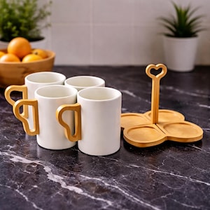 Könnte beinhalten: Ein Set aus drei Keramikbechern mit gesprenkelter, matter Oberfläche. Die Becher sind in Creme-, Hellgrau- und Dunkelgrautönen gehalten. Jeder Becher hat ein schlichtes, minimalistisches Design.