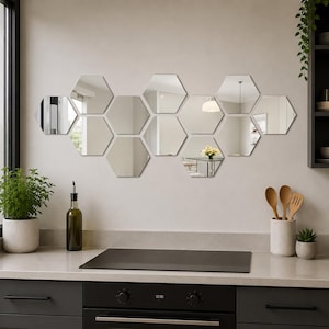 May include: A collection of hexagon-shaped mirrors arranged on a light gray wall. The mirrors reflect the surrounding room, including a table, a light fixture, and a window. The kitchen setting includes a black stovetop and dark gray cabinets.