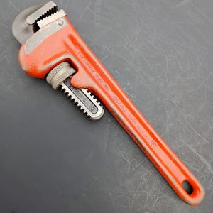 May include: An orange pipe wrench with a 10-inch capacity. The wrench has a toothed jaw and a textured handle for grip. The text "THE RIDGE TOOL CO. ELYRIA OHIO U.S.A. 10" is printed on the handle.