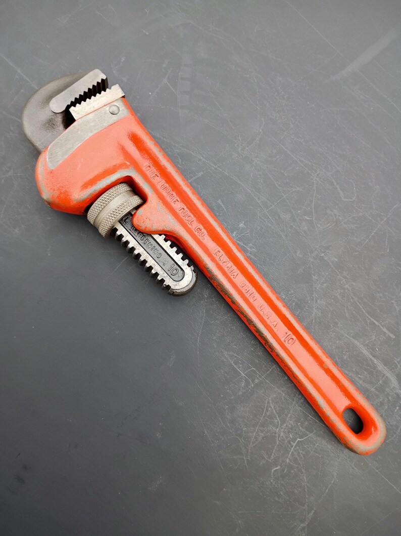 May include: An orange pipe wrench with a 10-inch capacity. The wrench has a toothed jaw and a textured handle for grip. The text "THE RIDGE TOOL CO. ELYRIA OHIO U.S.A. 10" is printed on the handle.