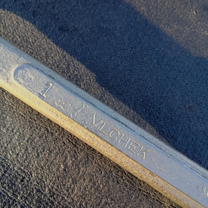May include: Close-up of a silver wrench with the number 1 and the brand name "VLCHEK" stamped on it. The wrench is made of metal and has a slightly worn appearance. The background is a dark, textured surface.