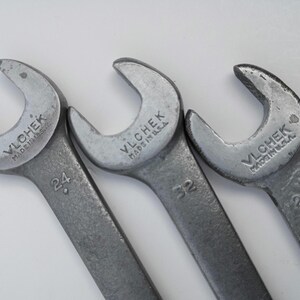 May include: Three silver Vlchek wrenches, Made in U.S.A., are arranged on a white surface. The wrenches have open ends and are marked with the numbers 24 and 32. The tools are for mechanical work.