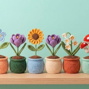 Puede incluir: Una colección de seis plantas de ganchillo en macetas individuales, que incluye una flor azul, dos azafranes morados, un girasol amarillo, un lirio de los valles blanco y una seta roja y blanca, con tallos y hojas verdes.