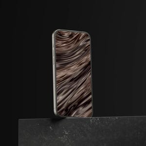 May include: A silver smartphone with a screen displaying a brown and black wavy pattern. The phone is positioned upright on a dark gray surface against a black background. The screen's design resembles flowing fur.