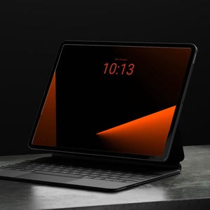 May include: A black tablet computer with a keyboard attachment, featuring a dark screen displaying the time 10:13 in red text. The screen background shows a geometric orange and black gradient design with sharp angular lines.