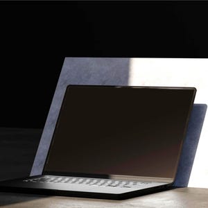 Könnte beinhalten: Ein schwarzer Laptop mit silberner Tastatur ist auf einer Oberfläche geöffnet und lehnt an einer weißen und grauen rechteckigen Struktur. Der Bildschirm ist dunkel und die Szene wird von natürlichem Licht beleuchtet.