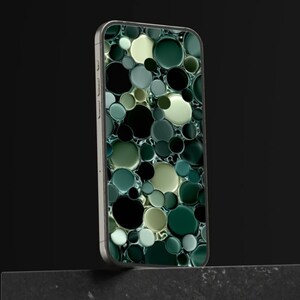 Peut inclure: Coque de smartphone avec un motif de cercles superposés dans des tons de vert, noir et crème. L'étui a un cadre argenté métallique et est présenté sur un fond sombre.