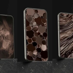 May include: Three smartphones with silver frames and different brown-toned screen designs. One displays a smoky pattern, another features a pattern of circles, and the third shows a wavy design. The phones are displayed on a dark surface.