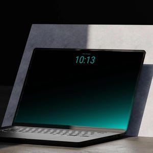 Könnte beinhalten: Ein schwarzer Laptop mit einem schmalen Displayrahmen, der die Uhrzeit 10:13 in einer türkisfarbenen digitalen Schrift anzeigt. Der Bildschirm hat einen dunklen Farbverlauf von Schwarz zu leuchtendem Türkis vor einer hellgrauen Platte.