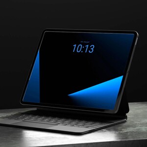 Könnte beinhalten: Ein Tablet mit schwarzem Bildschirm, der die Uhrzeit 10:13 in blauer Schrift anzeigt. Das Gerät ist mit einer schwarzen Tastaturhülle inklusive Trackpad verbunden. Der Bildschirm zeigt einen dunklen Hintergrund mit einer hellblauen Grafik.