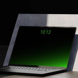 Könnte beinhalten: Ein schwarzer Laptop mit einem Display mit schmalem Rahmen, das einen grünen Farbverlauf und die digitale Uhrzeit 10:13 in grünem Text anzeigt. Das Gerät verfügt über eine Standardtastatur und ein dunkles Gehäuse vor einer hellen Fläche.