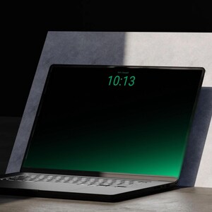 Könnte beinhalten: Ein schwarzer Laptop mit einem dunklen Bildschirm, der den grünen digitalen Text 10:13 anzeigt. Der Laptop verfügt über einen dünnen Rahmen und eine Tastatur mit sichtbaren Tasten und steht vor einer hellgrauen Platte.
