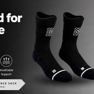 Puede incluir: Calcetines deportivos negros y blancos con un logotipo. El texto "Engineered for Every Move" y "Built to Perform" es visible. Características: absorción de la humedad, comodidad acolchada, diseño duradero y soporte transpirable.