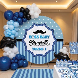 Könnte beinhalten: Eine Geburtstagsparty-Szene mit blauen und weißen Luftballons, einem großen runden Hintergrund mit dem Text "BOSS BABY Daniel's TURNS 1" und passenden Partyartikeln. Das Farbschema ist blau, weiß und schwarz, mit einem Schnurrbart-Thema.