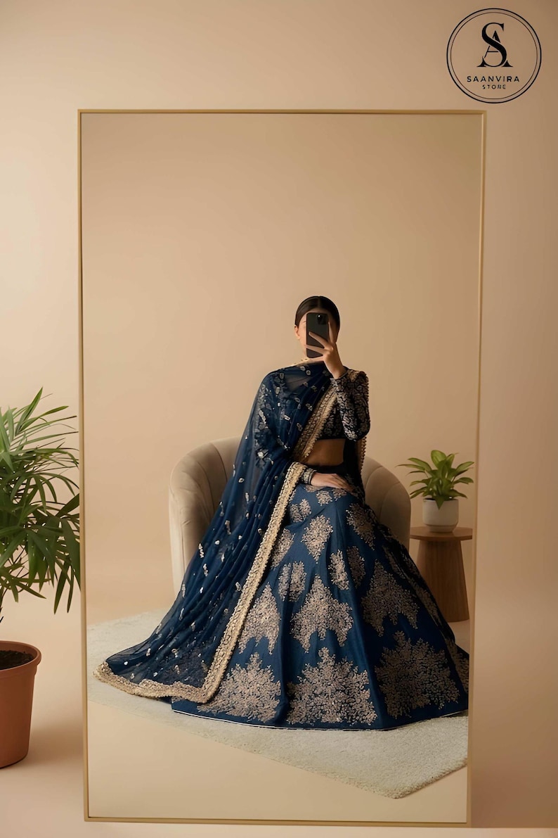 May include: A navy blue lehenga with gold embroidery, a matching dupatta, and a long-sleeved blouse. The outfit is reflected in a large mirror. The Saanvira Store logo is in the upper right corner. The outfit is suitable for special occasions.