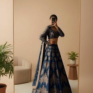 May include: A navy blue lehenga with gold floral embroidery. The long-sleeved blouse and skirt feature intricate patterns. The outfit is reflected in a large mirror, with the Saanvira Store logo visible in the top right corner.