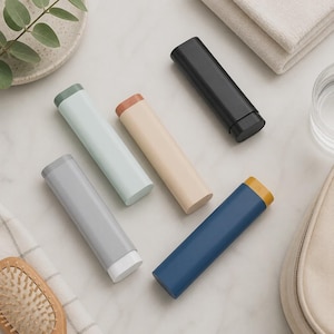 Könnte beinhalten: Fünf zylindrische Etuis in verschiedenen Farben, darunter Schwarz, Marineblau mit gelber Kappe, Hellblau, Beige mit brauner Kappe und Grau mit weißer Kappe. Jedes Etui hat eine glatte, matte Oberfläche und eine abgerundete rechteckige Form.
