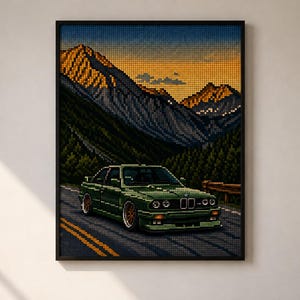 May include: A framed pixel art print featuring a dark green coupe driving on a mountain road. The background displays a sunset over jagged, snow-capped peaks and a dense forest. The artwork uses a grid-like aesthetic to depict the car and landscape.