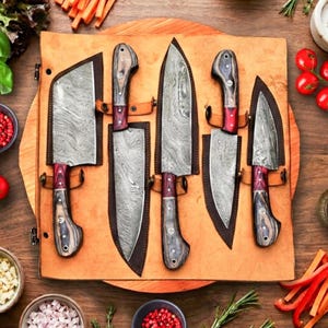 Puede incluir: Un juego de cinco cuchillos de cocina de acero de Damasco con mangos de madera y detalles rojos, exhibidos en una funda de cuero. Los cuchillos están dispuestos sobre una tabla de cortar de madera, rodeados de ingredientes.