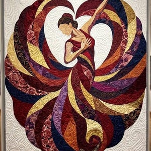 Op de afbeelding: Een rechthoekige wandquilt met een centrale applicatie van een danser in een zwierige jurk. De jurk is samengesteld uit gebogen stoffen panelen in tinten rood, bordeaux, goud en paars met rozenpatronen, tegen een witte gewatteerde achtergrond.