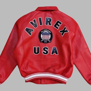 Premium Avirex USA red leather jacket with embroidered logo detailing, classic bomber style, ribbed cuffs and hem, high-quality craftsmanship.