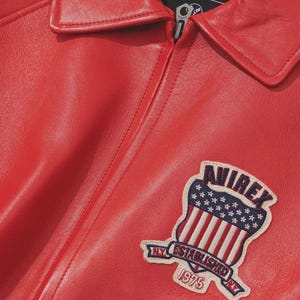 Premium Avirex USA red leather jacket with embroidered logo detailing, classic bomber style, ribbed cuffs and hem, high-quality craftsmanship.