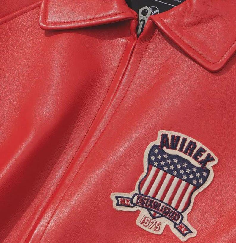 Premium Avirex USA red leather jacket with embroidered logo detailing, classic bomber style, ribbed cuffs and hem, high-quality craftsmanship.