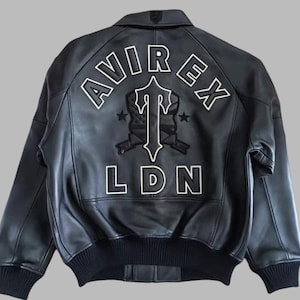 Black Avirex leather jacket featuring bold embroidered Avirex LDN lettering on the back, classic bomber style, ribbed cuffs and hem, premium craftsmanship.