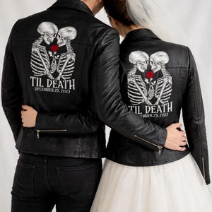 Puede incluir: Chaquetas de cuero negras con diseño de esqueleto y rosa. Las chaquetas tienen el texto "TIL DEATH DECEMBER 25, 2023". Una persona lleva un vestido de novia blanco y la otra vaqueros negros.
