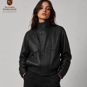 以下が含まれることがあります： 黒い革のジャケット。ハイカラーとボタン留め。ジャケットはリブ編みの裾とテーラードフィットです。The Leather Workshopのロゴが見えます。