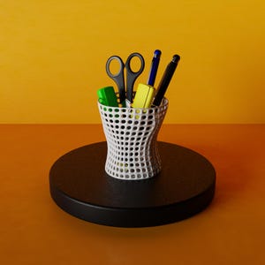 May include: A white, perforated pen holder containing black scissors, a blue pen, a black pen, a green highlighter, and a yellow highlighter. The pen holder sits on a black, round platform against an orange background.