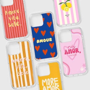 Op de afbeelding: Een verzameling doorzichtige telefoonhoesjes met kleurrijke ontwerpen. De hoesjes tonen zinnen als "Amore, Vita, Sole" en "More Amor". Ontwerpen omvatten rode strepen, blauwe harten en gele strepen. De hoesjes zijn ontworpen voor een smartphone.