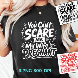 Op de afbeelding: Een zwart t-shirt met witte grafische tekst die luidt: You Can't SCARE Me My Wife is PREGNANT, geaccentueerd met kleine sterren en bliksemschichtsymbolen. Het ontwerp is gecentreerd op de borst, met extra variaties in de hoeken.