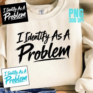 以下が含まれることがあります： 胸元に太い筆致のフォントで「I Identify As A Problem」という黒いテキストがプリントされた、クリーム色のクルーネックトレーナー。長袖で、襟の内側にはGildanブランドのタグが見えています。
