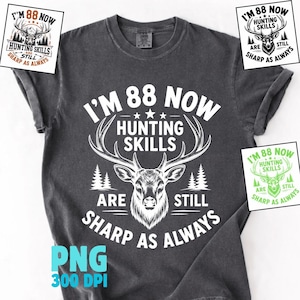 May include: A charcoal grey t-shirt featuring a white graphic of a deer head with antlers, pine trees, and the text I'M 88 NOW HUNTING SKILLS ARE STILL SHARP AS ALWAYS. The design includes three stars above the deer and is centred on the chest.