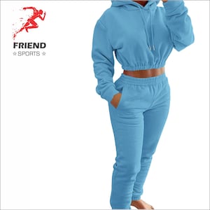 Peut inclure: Ensemble de survêtement bleu clair composé d'un sweat à capuche court avec cordon de serrage et d'un pantalon de survêtement assorti avec poches. Le logo "FRIEND SPORTS" est visible en haut à gauche.