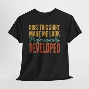 May include: A black short-sleeved t-shirt featuring the text "DOES THIS SHIRT MAKE ME LOOK Professionally DEVELOPED" printed in yellow, teal, and orange block and script lettering on the front centre of the garment.