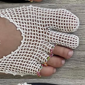 May include: A pair of off-white crochet toe socks featuring a net-like pattern and individual toe compartments with small colorful beads at the tips. The socks are worn with black thong sandals and include the text made in this tutorial.