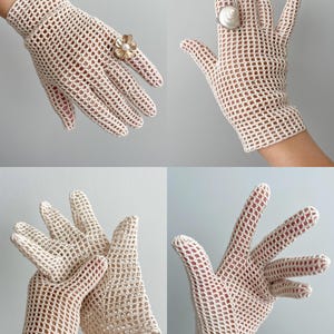 K&ouml;nnte beinhalten: Cremefarbene H&auml;kelhandschuhe mit offenem Gewebe. Die Handschuhe werden in mehreren Ansichten gezeigt, mit einem Blumenring und einem Muschelring an den Fingern. Die Handschuhe haben ein zartes, spitzenartiges Aussehen, und das offene Gewebe l&auml;sst die Haut sichtbar werden.