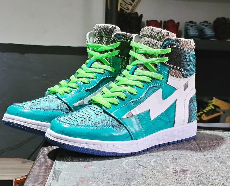 Pu&ograve; includere: Un paio di sneakers alte turchesi e bianche con un design a fulmine. Le scarpe hanno lacci verdi e una texture simile alla pelle di serpente sulla tomaia. Le suole sono bianche con la parte inferiore blu.