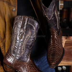 Peut inclure: Deux bottes de cowboy marron, avec un motif peau de serpent sur la partie inférieure et un motif brodé plus foncé sur la tige supérieure. Les bottes ont des bouts pointus et des talons empilés, de style Western.
