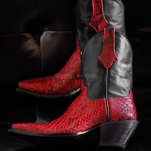 May include: Cowboy boots featuring a red snakeskin design on the foot and a black leather upper. These boots have a pointed toe and a stacked heel. The overall design offers a bold, Western-inspired aesthetic.