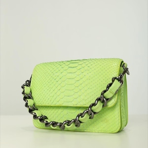 May include: A neon green handbag with a chain strap. The bag has a textured, snakeskin-like pattern. The chain strap is a dark gunmetal color, and the bag is rectangular in shape.