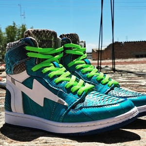 Pu&ograve; includere: Un paio di sneakers alte turchesi e bianche, con un design a fulmine. Le scarpe hanno lacci verde brillante e una texture simile alla pelle di serpente sulla tomaia. Le suole sono bianche con un accento blu.