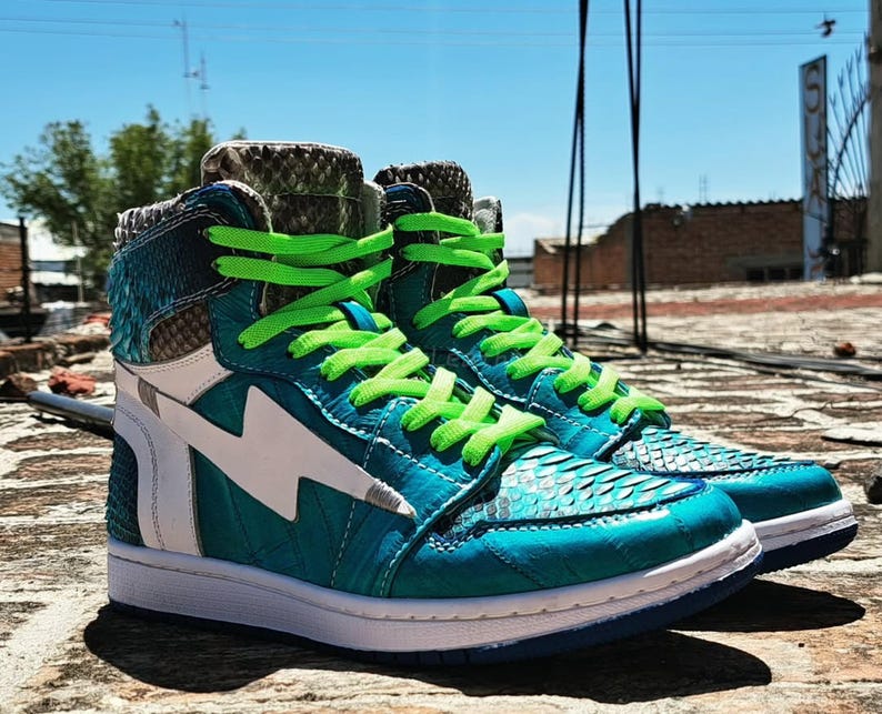 Pu&ograve; includere: Un paio di sneakers alte turchesi e bianche, con un design a fulmine. Le scarpe hanno lacci verde brillante e una texture simile alla pelle di serpente sulla tomaia. Le suole sono bianche con un accento blu.