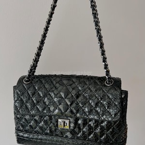 Può includere: Borsa in pelle trapuntata nera con tracolla a catena argentata. La borsa presenta un motivo a rombi e una chiusura con fermaglio argentato. La borsa è tenuta da una tracolla a catena argentata.