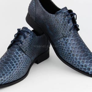 May include: A pair of blue leather dress shoes with a textured snakeskin pattern. The shoes have a pointed toe, a lace-up closure, and a low heel. The shoes are displayed on a white background.