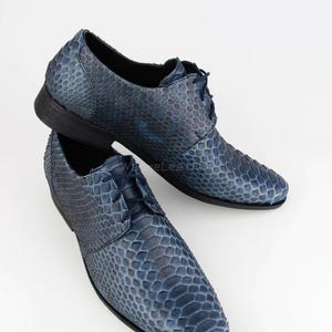May include: A pair of blue leather dress shoes with a snakeskin pattern. The shoes have a lace-up design and a dark sole. The shoes are displayed on a white background.