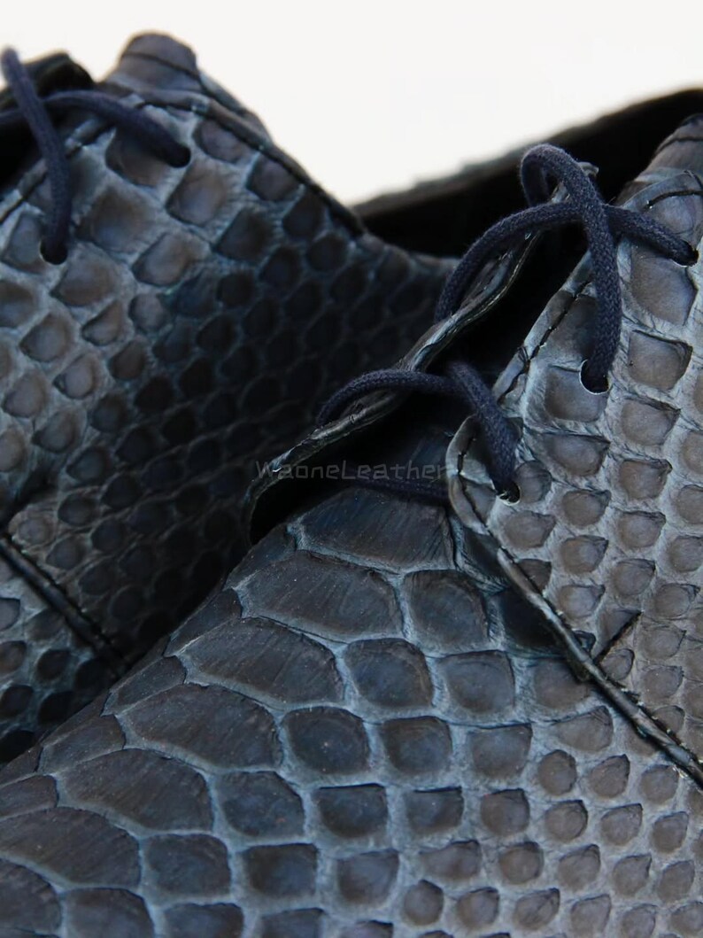 May include: Close-up of a pair of dark blue leather shoes with a scale-like texture. The shoes have matching blue laces and a classic lace-up design. The leather appears to be high-quality, with visible texture and detail.